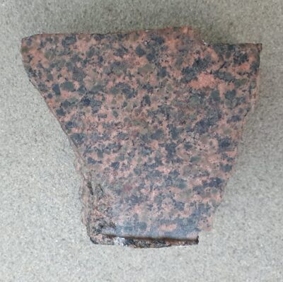 A polished piece of Markfieldite, approximately 5 cm across, showing pink, green, and black minerals. From OUMNH.