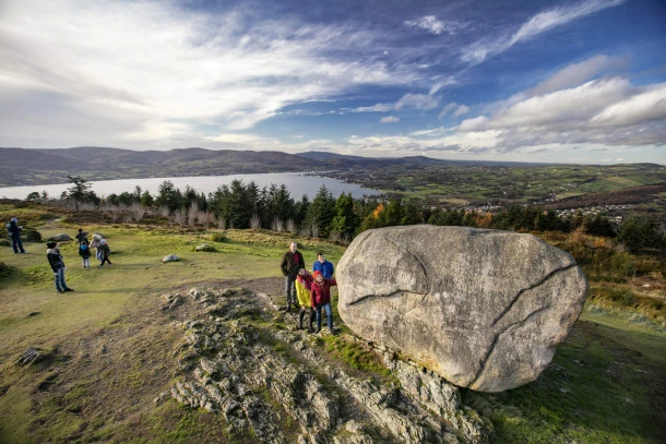 A large boulder near the top of a hill. People stand around the boulder looking at it