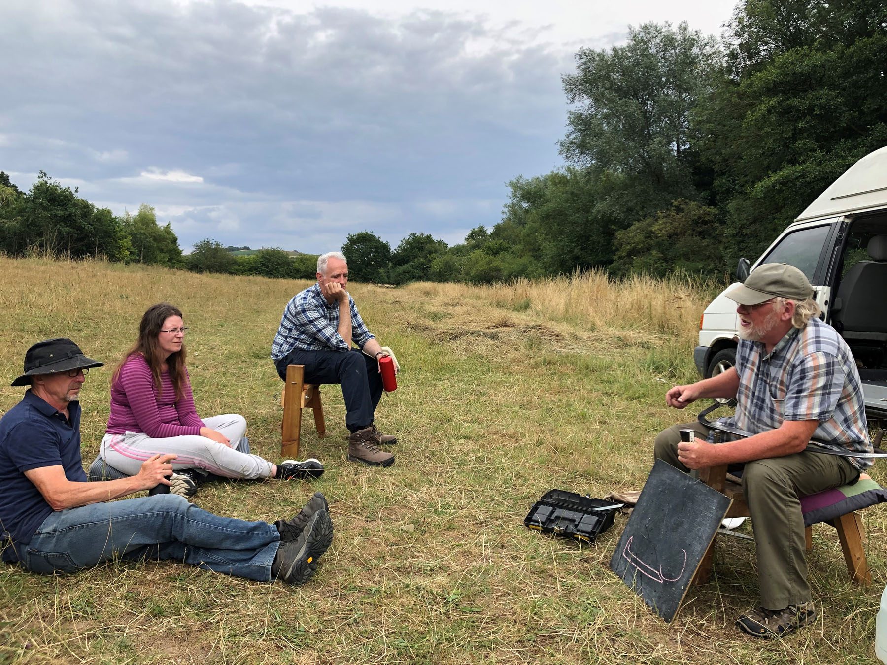 A group meets in a field, in summer, for scything training