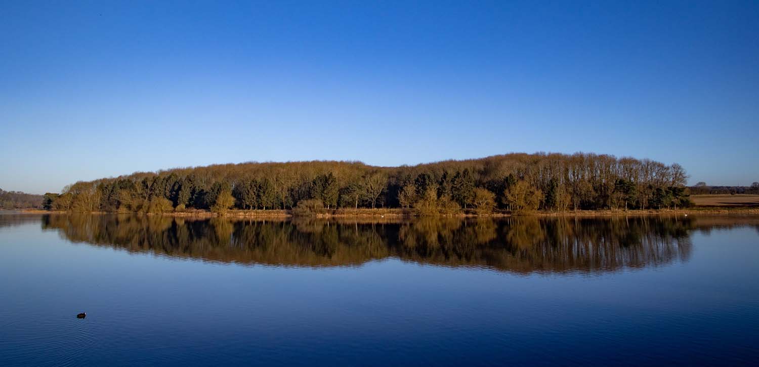 An autumn day at Thornton Reservoir. The trees on the opposite side of the lake are reflected in the very still water.